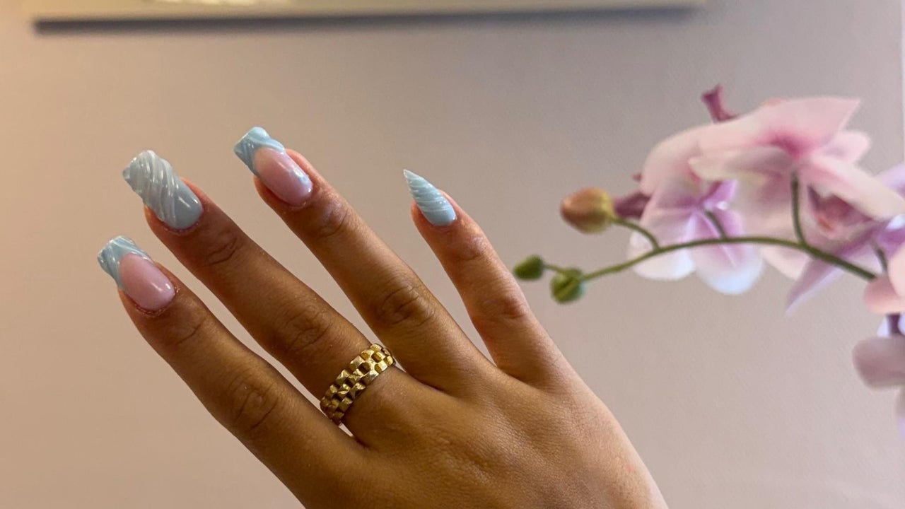 Gel-X nagels met een lichtblauwe french en een gouden ring, naast een roze orchidee